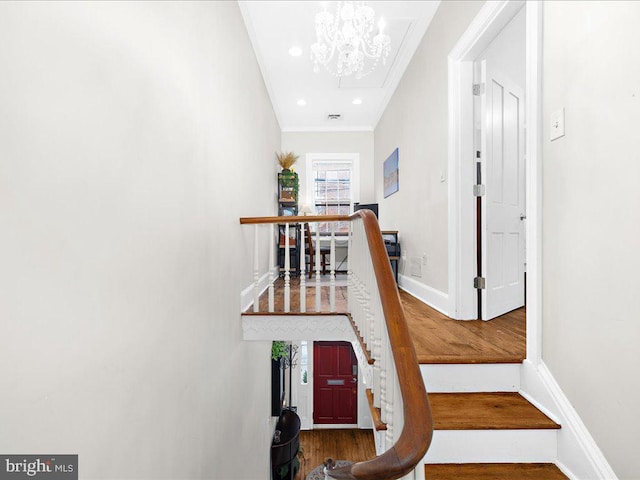 stairs with wood-type flooring, ornamental molding, and a chandelier