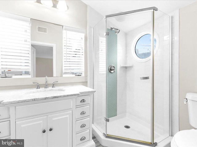 bathroom with vanity, toilet, a shower with door, and a wealth of natural light