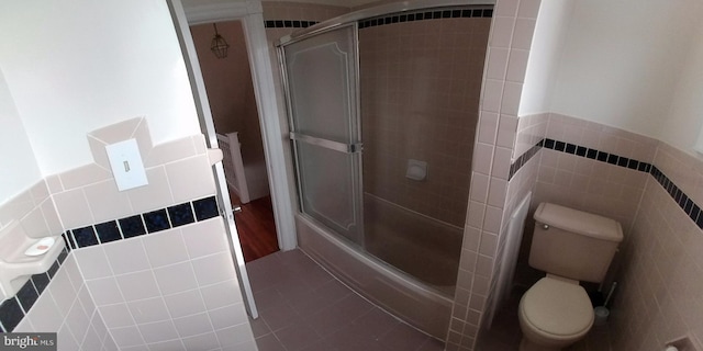 bathroom featuring bath / shower combo with glass door, toilet, tile patterned flooring, and tile walls