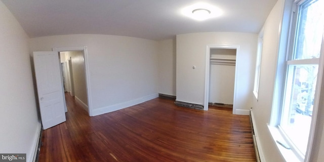 unfurnished bedroom featuring baseboard heating, dark hardwood / wood-style flooring, and a closet