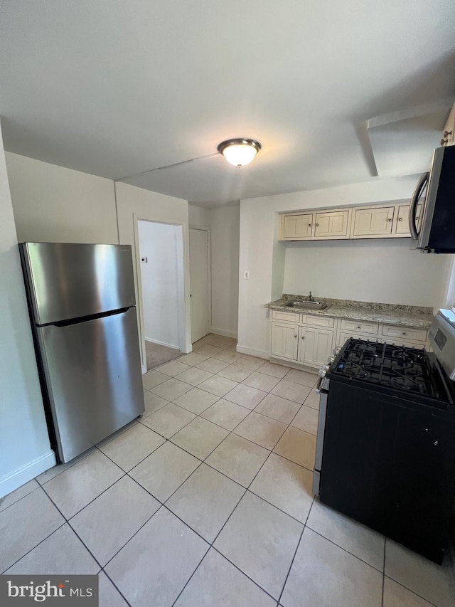 kitchen featuring sink, light tile patterned floors, stainless steel appliances, light stone countertops, and cream cabinetry