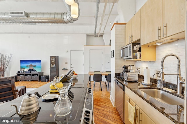 kitchen with sink, appliances with stainless steel finishes, dark stone countertops, decorative backsplash, and light brown cabinets