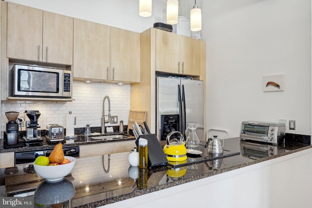 kitchen featuring stainless steel appliances, decorative light fixtures, sink, and dark stone countertops