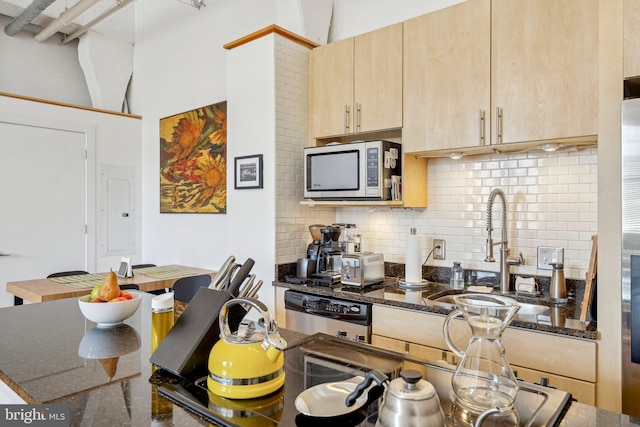 kitchen with light brown cabinetry, sink, dark stone countertops, stainless steel appliances, and backsplash