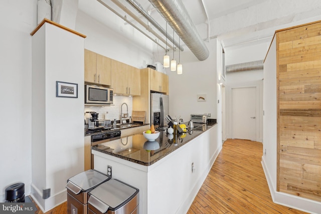 kitchen featuring appliances with stainless steel finishes, a towering ceiling, pendant lighting, sink, and dark stone countertops