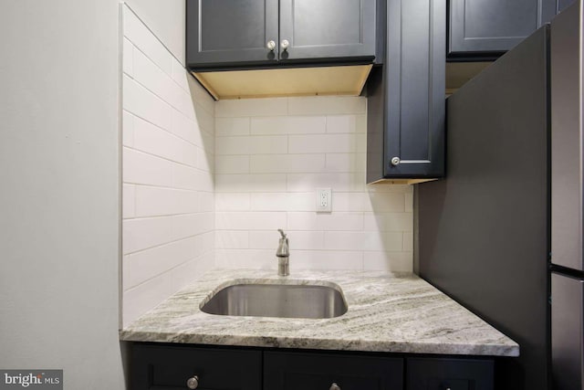 kitchen featuring tasteful backsplash, stainless steel fridge, light stone countertops, and sink