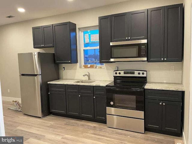 kitchen with light stone countertops, appliances with stainless steel finishes, sink, and light hardwood / wood-style floors