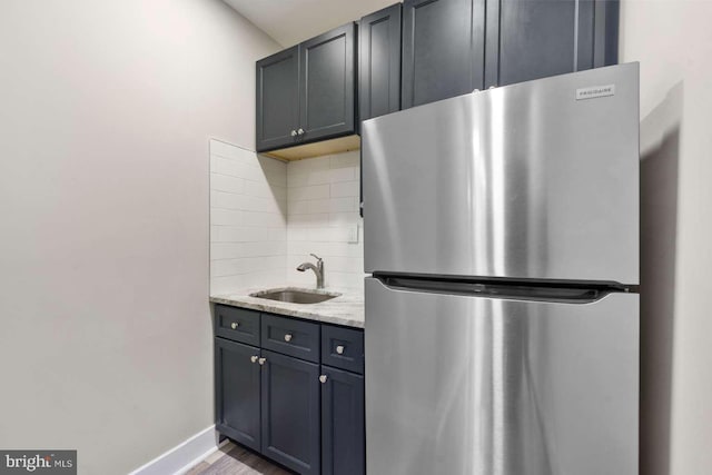 kitchen featuring gray cabinets, sink, stainless steel fridge, backsplash, and light stone countertops