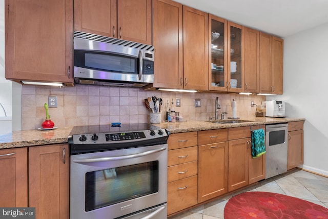 kitchen with light stone countertops, sink, backsplash, appliances with stainless steel finishes, and light tile patterned flooring