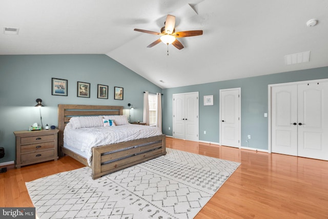 bedroom featuring ceiling fan, two closets, wood-type flooring, and lofted ceiling