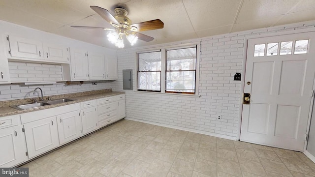 kitchen with sink, ceiling fan, white cabinets, and brick wall