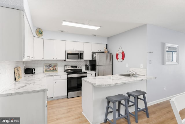 kitchen with sink, a kitchen breakfast bar, kitchen peninsula, stainless steel appliances, and white cabinets