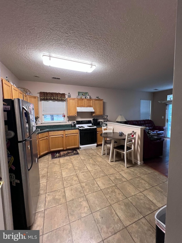 kitchen featuring a textured ceiling, gas stove, stainless steel refrigerator, and light tile patterned flooring