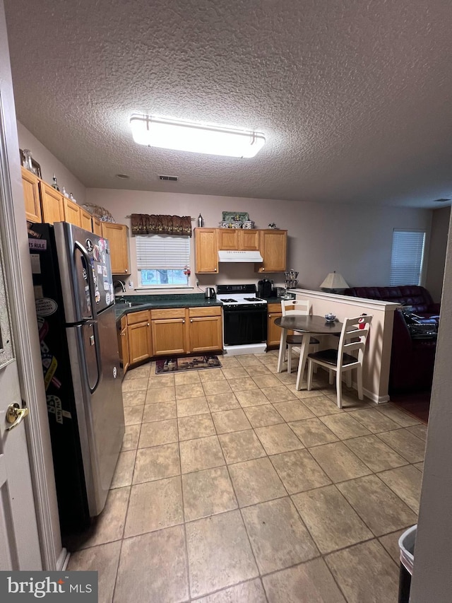 kitchen with gas stove, light tile patterned floors, a textured ceiling, and stainless steel refrigerator