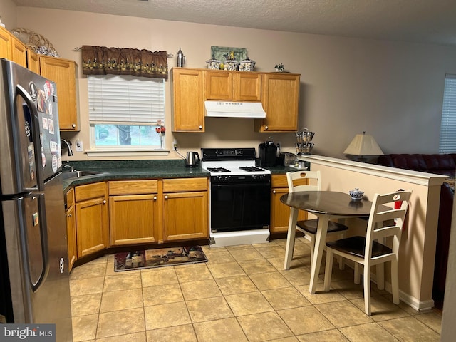 kitchen with light tile patterned floors, sink, stainless steel fridge, a textured ceiling, and range with gas cooktop