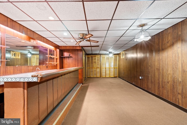 bar featuring light carpet, wooden walls, ceiling fan, and a paneled ceiling