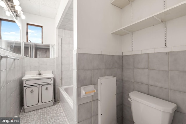 bathroom with tile walls, tiled tub, vanity, and toilet