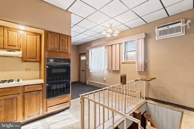 kitchen featuring double oven, a wall unit AC, carpet flooring, a drop ceiling, and white gas cooktop