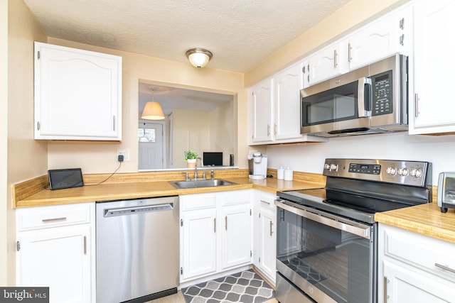 kitchen featuring white cabinetry, appliances with stainless steel finishes, sink, and decorative light fixtures