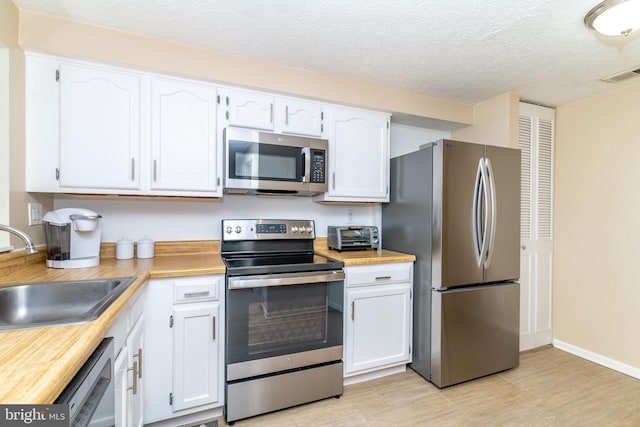 kitchen with appliances with stainless steel finishes, sink, white cabinets, and a textured ceiling