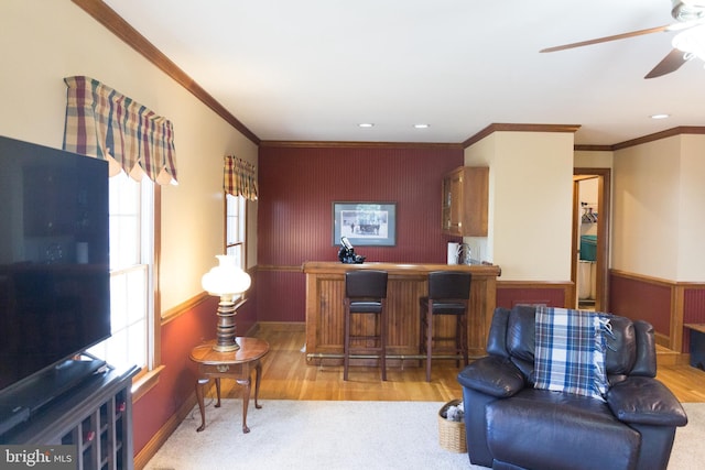 living room with bar, crown molding, light hardwood / wood-style flooring, and ceiling fan