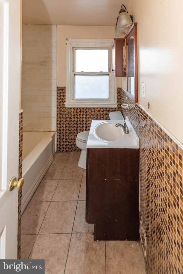 bathroom with tile walls, a bathtub, vanity, tile patterned floors, and toilet