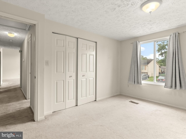 unfurnished bedroom with carpet floors, a textured ceiling, a closet, baseboards, and attic access