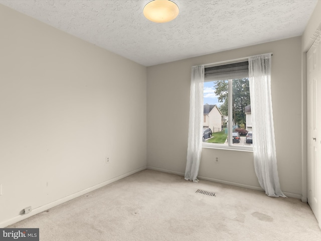 unfurnished room featuring light carpet, a textured ceiling, and baseboards