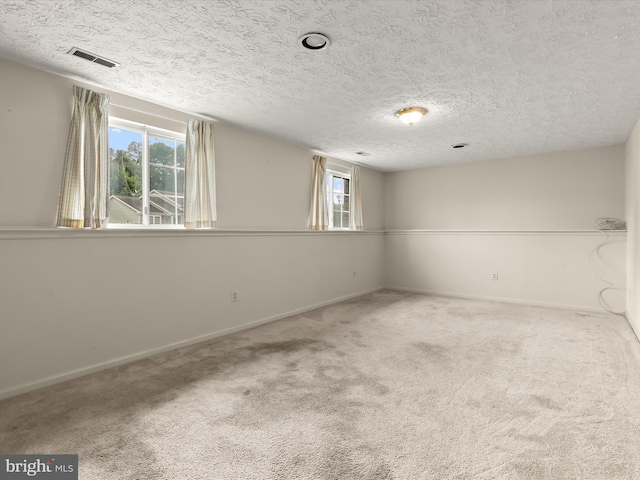 carpeted spare room with plenty of natural light, a textured ceiling, and baseboards
