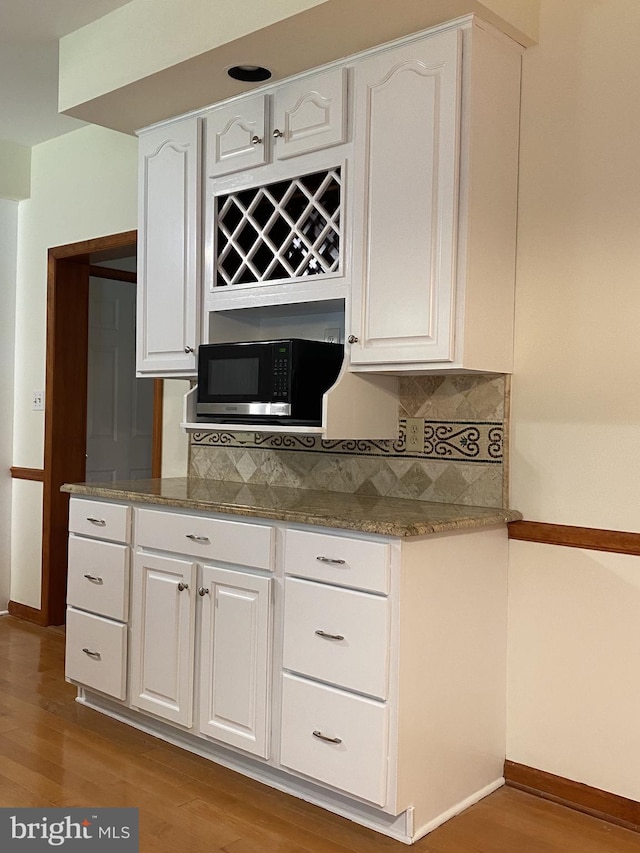 kitchen featuring white cabinetry, hardwood / wood-style floors, decorative backsplash, and stone counters