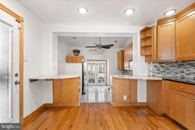 kitchen with light wood-type flooring, kitchen peninsula, stainless steel appliances, light stone countertops, and decorative backsplash