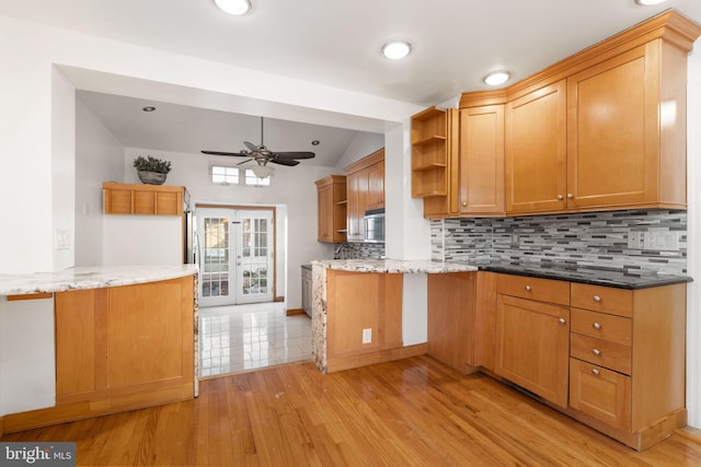 kitchen with lofted ceiling, backsplash, kitchen peninsula, light stone countertops, and light hardwood / wood-style flooring