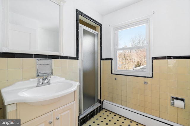 bathroom featuring baseboard heating, vanity, a shower with door, and tile walls