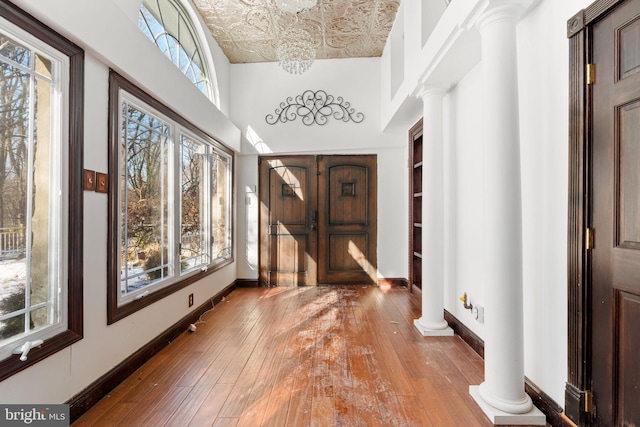 entryway with a towering ceiling, wood-type flooring, a chandelier, and ornate columns