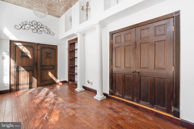 entryway featuring decorative columns, wood-type flooring, and a towering ceiling