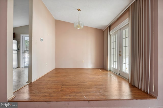 empty room featuring french doors, lofted ceiling, light hardwood / wood-style floors, and a notable chandelier