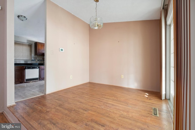 unfurnished room with a wealth of natural light, a notable chandelier, and light hardwood / wood-style flooring