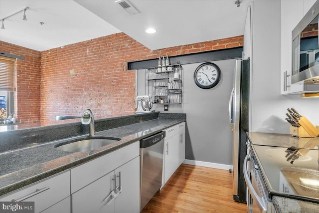 kitchen featuring appliances with stainless steel finishes, brick wall, white cabinetry, sink, and hanging light fixtures