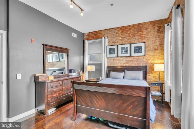 bedroom with brick wall, dark hardwood / wood-style floors, and track lighting