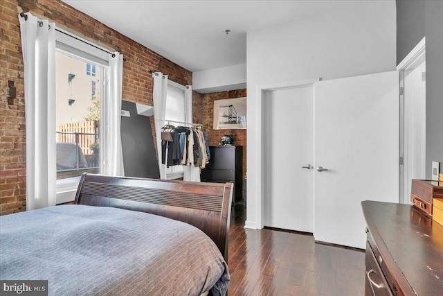 bedroom with dark wood-type flooring, brick wall, and a closet