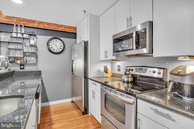 kitchen with white cabinetry, appliances with stainless steel finishes, dark stone countertops, and light wood-type flooring