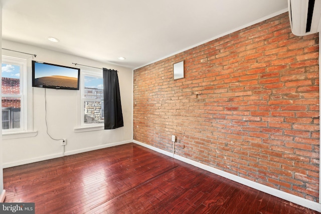 spare room featuring wood-type flooring and brick wall