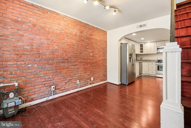 unfurnished living room with dark hardwood / wood-style flooring, sink, and brick wall