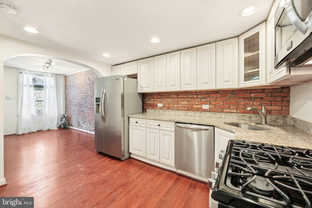 kitchen with sink, appliances with stainless steel finishes, dark hardwood / wood-style floors, light stone counters, and brick wall