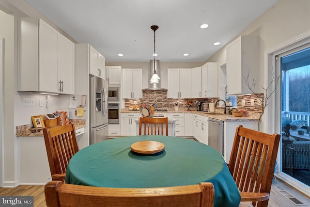 kitchen featuring wall chimney range hood, sink, white cabinetry, stainless steel appliances, and decorative light fixtures