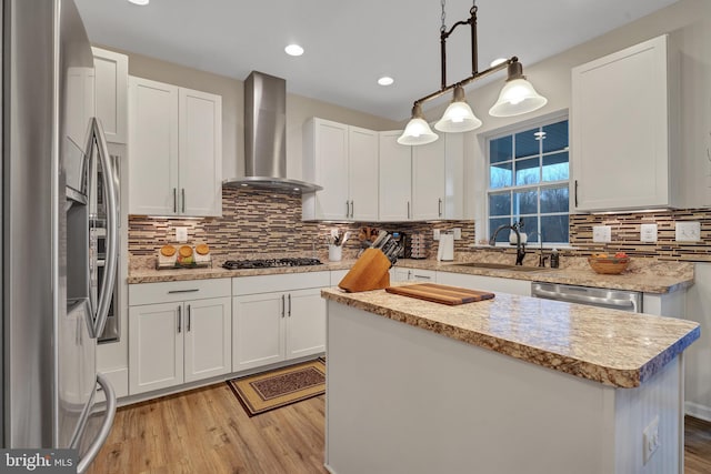 kitchen with pendant lighting, wall chimney range hood, sink, appliances with stainless steel finishes, and white cabinetry