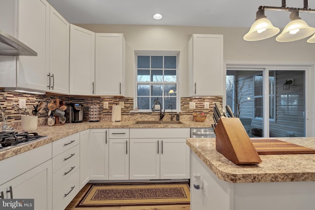 kitchen with tasteful backsplash, sink, white cabinets, hanging light fixtures, and exhaust hood