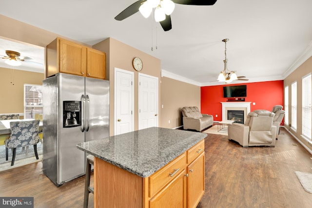 kitchen with stainless steel fridge, ornamental molding, a center island, and dark stone counters