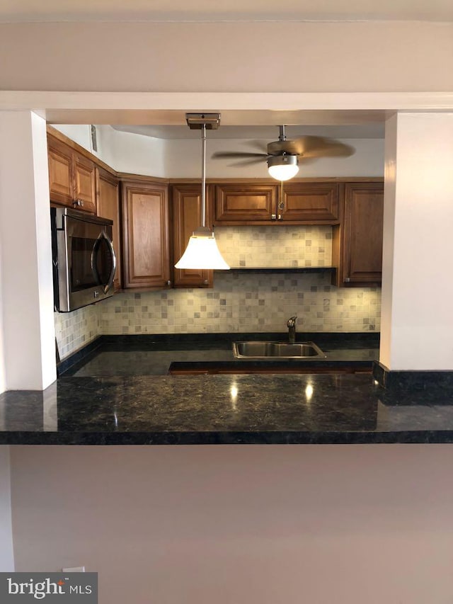 kitchen with pendant lighting, sink, dark stone countertops, backsplash, and kitchen peninsula