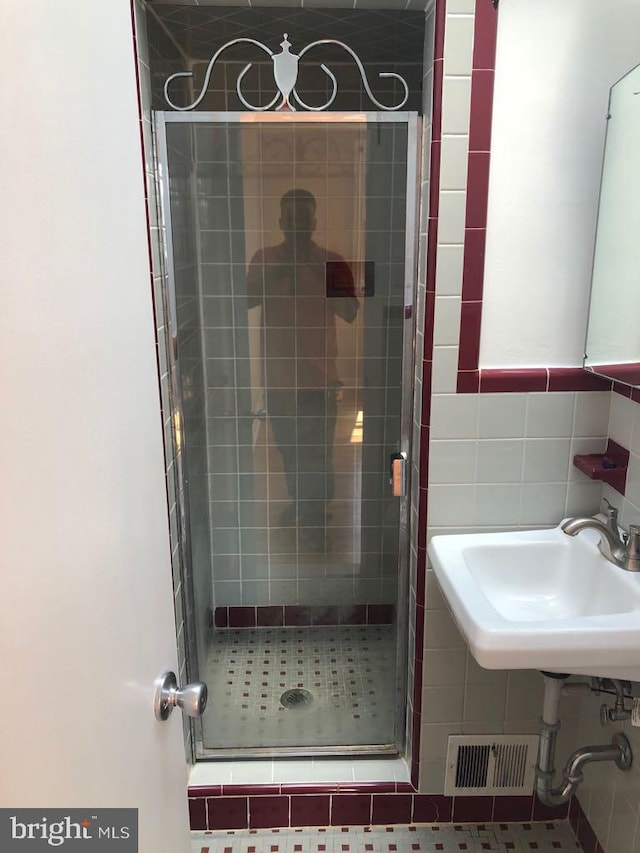 bathroom featuring tile patterned flooring, sink, a shower with shower door, and tile walls